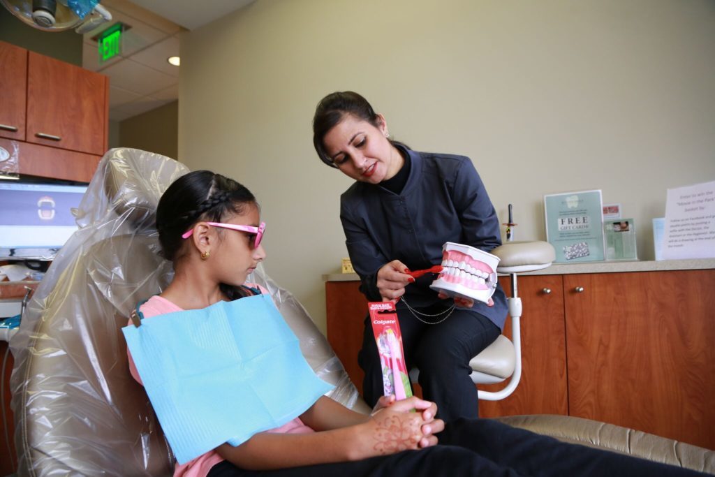 Hygienist in Renton Smile showing a young pediatric dentistry patient how to properly brush teeth on model. 