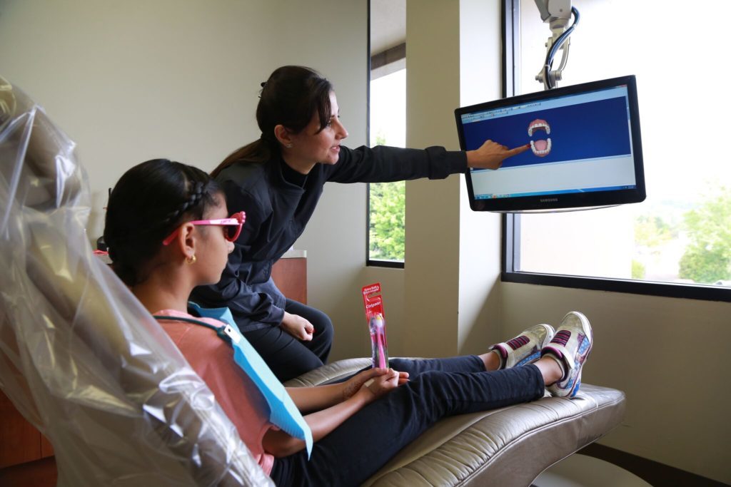 A child patient looking at a 3D rendering of her mouth to shoe areas where general dentistry services like cleaning will help her maintain good oral health. 